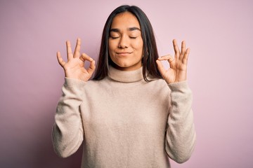 Young beautiful asian woman wearing casual turtleneck sweater over pink background relax and smiling with eyes closed doing meditation gesture with fingers. Yoga concept.