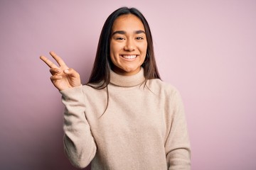 Young beautiful asian woman wearing casual turtleneck sweater over pink background showing and pointing up with fingers number two while smiling confident and happy.