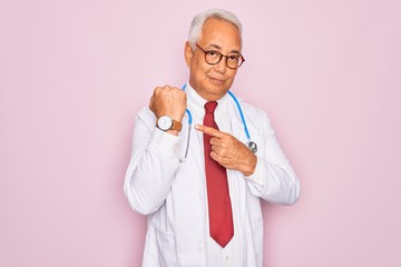 Middle age senior grey-haired doctor man wearing stethoscope and professional medical coat In hurry pointing to watch time, impatience, looking at the camera with relaxed expression