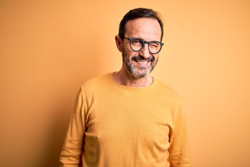 Middle age hoary man wearing casual sweater and glasses over isolated yellow background winking...