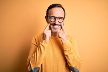 Middle age hoary man wearing casual sweater and glasses over isolated yellow background Smiling with open mouth, fingers pointing and forcing cheerful smile