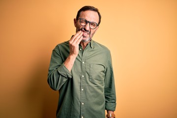 Fototapeta premium Middle age hoary man wearing casual green shirt and glasses over isolated yellow background touching mouth with hand with painful expression because of toothache or dental illness on teeth. Dentist