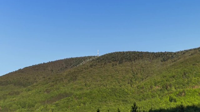 Zoom in hyperlapse tower timelapse of shadows and clouds moving on Radhost Hill overlooking a tower in a dense forest with moving shadows reflecting the sun from clouds Beskydy Park area.