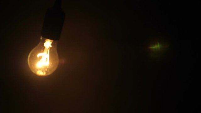 Classic glass lamp with tungsten filament flicker lights up, swaying on the wire on a black background. Closeup. Slow mo, slo mo, slow motion, high speed camera
