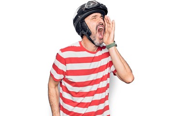 Middle age handsome motorcyclist man wearing moto helmet over isolated white background shouting and screaming loud to side with hand on mouth. Communication concept.