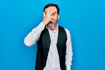 Middle age handsome man wearing elegant shirt and vest over isolated blue background peeking in...