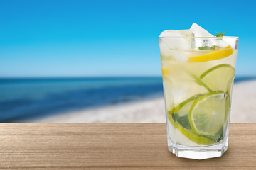 Citrus lemonade with ice cubes on wooden table at beach, space for text