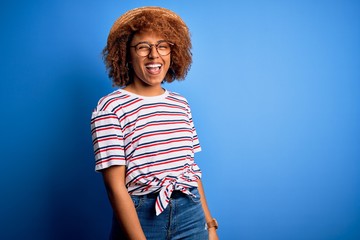 African American woman with curly hair on vacation wearing summer hat and striped t-shirt winking...