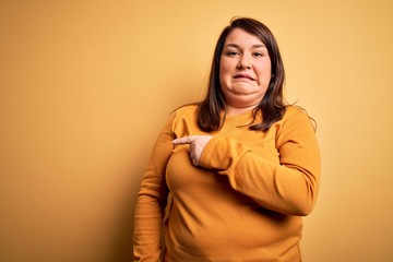 Beautiful brunette plus size woman wearing casual sweater over isolated yellow background Pointing aside worried and nervous with forefinger, concerned and surprised expression