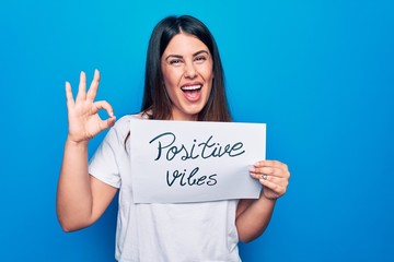 Young beautiful woman asking for optimist attitude holding paper with positive vibes message doing ok sign with fingers, smiling friendly gesturing excellent symbol