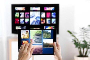 Streaming video services. Woman using tablet to change channels on TV, closeup