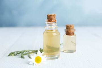 Bottles of essential oil and fresh chamomile on white wooden table