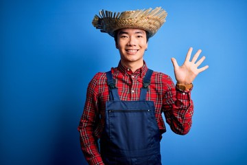 Young handsome chinese farmer man wearing apron and straw hat over blue background showing and...