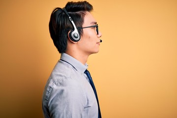 Young handsome chinese call center agent man wering glasses using headset looking to side, relax...
