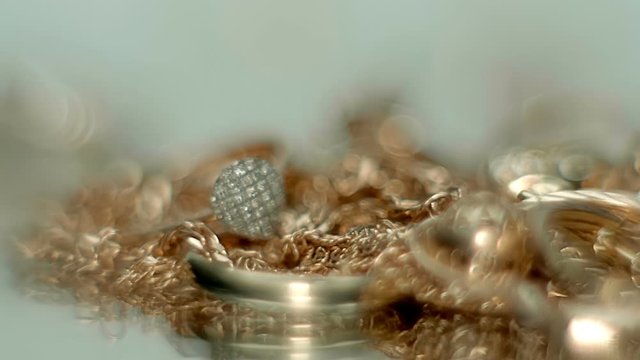 Beautiful shiny, sparkling golden jewelry fall on a glass surface with bright flares. Macro. Closeup. Shallow depth of field. Slow mo, slo mo, slow motion, high speed camera