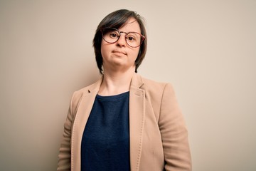 Young down syndrome business woman wearing glasses standing over isolated background Relaxed with serious expression on face. Simple and natural looking at the camera.