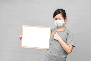 Little asian girl in a protective medical mask holding whiteboard isolated on gray background....