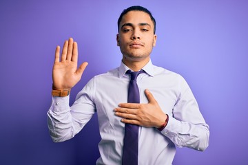 Young brazilian businessman wearing elegant tie standing over isolated purple background Swearing with hand on chest and open palm, making a loyalty promise oath