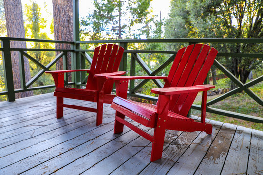 Red Adirondack Chairs Serenely Sitting Outside A Cabin In The Forest