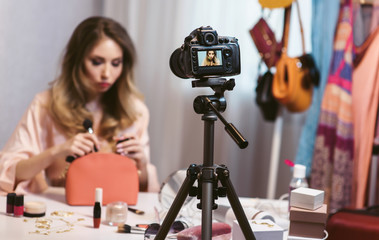 Famous blogger recording vlog at home. Young attractive woman fashion vlogger talking to the camera about her new makeup bag and cosmetics. Blogging as a lifestyle of modern women. Focus at camera