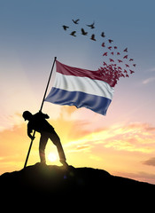 Netherlands flag turn to birds while being planted by a man on a hill during sunrise.