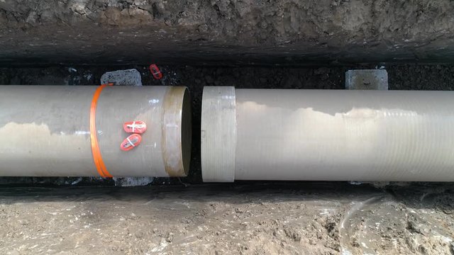 Concrete pipe tube installation. Aerial above men at work outside with heavy machinery to connect and install water or sewerage pipeline in a digging soil land
