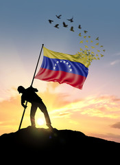 Venezuela flag turn to birds while being planted by a man on a hill during sunrise.