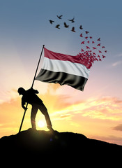 Yemen flag turn to birds while being planted by a man on a hill during sunrise.