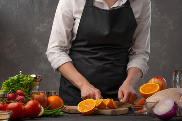 Cooking festive chicken for baking, the chef cuts an orange against a background of vegetables and fruits. Recipe book and gastronomy