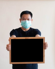 asian man in a protective medical mask holding blackboard isolated on gray background. Protect from...