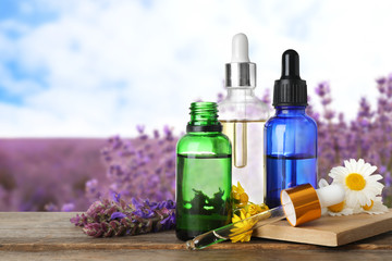 Bottles of essential oils and wildflowers on wooden table against blurred background. Space for text