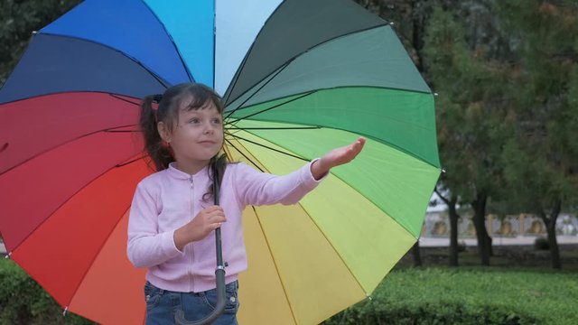 Child catch drops. Adorable little girl in the rain with a large multi-colored umbrella.