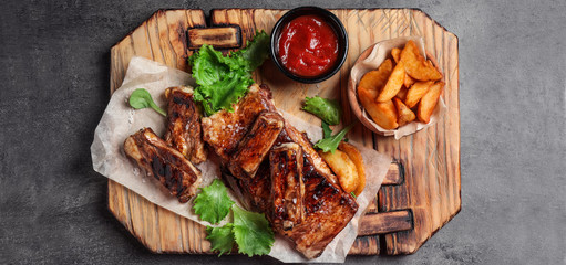 Delicious grilled ribs and garnish on grey table, top view. Banner design