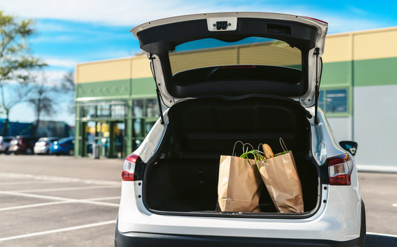 Groceries from a supermarket in a car trunk. Social distancing. Food delivery during quarantine. Paper eco bags for shopping