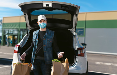 A courier in a protective mask and medical gloves delivers grocery bags from the supermarket. Auto...