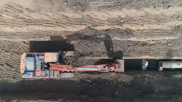 Drone above excavating bulldozer or tractor digging and land cleaning soil land. Men at work outdoor outside with heavy machinery loading arm installing water pipeline
