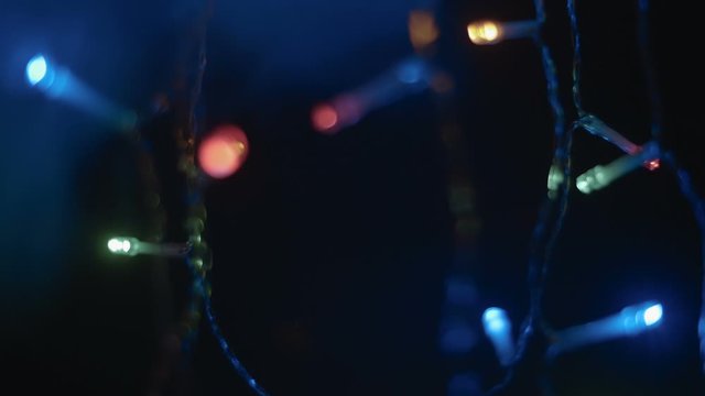 Bright multi-colored garland hanging in the dark and glowing. The camera moves around