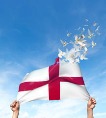 Two hands are holding an England flag which morphs into birds while waving against a blue sky background. 3D Illustration.