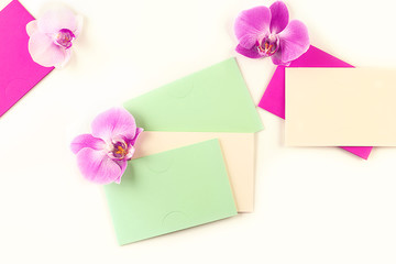 Orchid flowers, green, pink and violet envelopes on a light background. Minimal composition. Mock-up, creative minimalism, flat lay. Top view, copy space.
