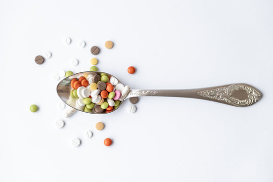 Medicine and health, treatment, pharmaceutics, coronavirus, pandemic, epidemic concept - layout one silver big tablespoon with multi-colored tablets and capsules on a white background copy space.