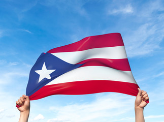 Fototapeta premium Two hands are holding a Puerto Rico flag - flowing through the wind. 3D Illustration.