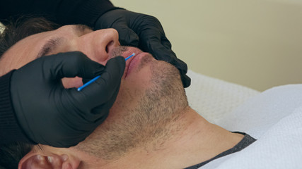 High quality close-up of a man laying on a couch during the esthetician lips treatment. Male...