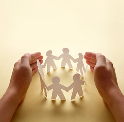 Paper people surrounded by hands in gesture of protection. Concept of insurance, social protection...
