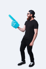 Full length photo bearded hipster man wearing sunglasses and pointing with big fan glove over white