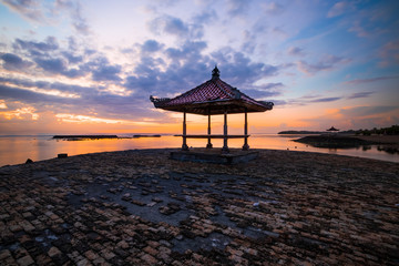 Sunrise seascape. Traditional balinese gazebos. Cloudy sky. Sunlight at horizon. Nusa Dua beach, Bali, Indonesia.