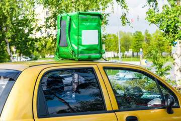 Green food delivery backpack standing on the top of yellow car. Mockup box for food delivery service. Copy space.