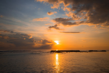 Naklejka na ściany i meble Rising sun at horizon. Sunrise seascape. Amazing water reflection. Cloudy sky. Sunlight at horizon. Nusa Dua beach, Bali, Indonesia.