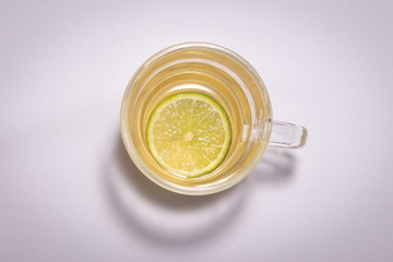 Chá de Camomila com Limão na xícara grande de vidro transparente com lindo vaso de flor amarela sobre a mesa branca