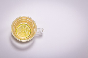 Chá de Camomila com Limão na xícara grande de vidro transparente com lindo vaso de flor amarela sobre a mesa branca