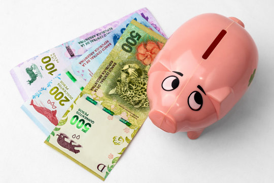 Alcanc&iacute;a chanchito vista cenital junto a billetes de pesos argentinos distribuidos en forma de abanico sobre fondo blanco